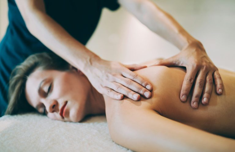 A bride on her wedding day receiving a back massage in a tranquil setting.