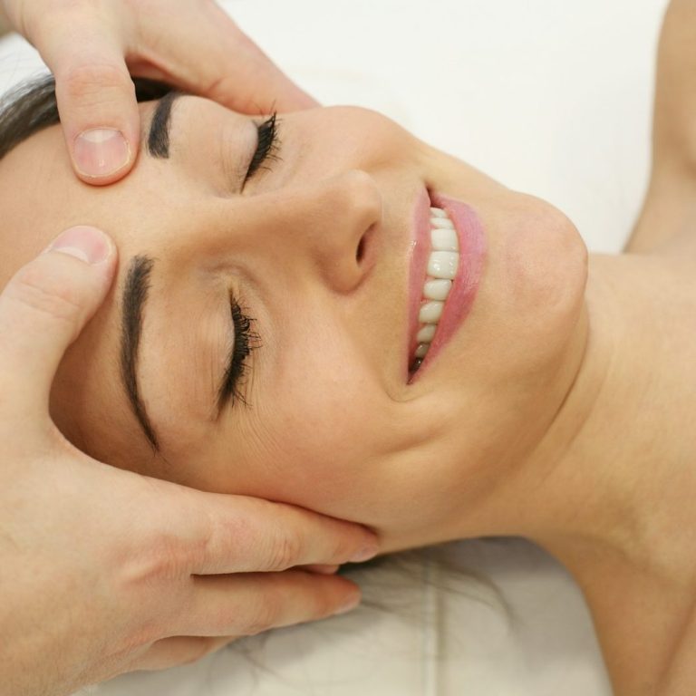 A relaxed woman enjoying a facial massage with gentle hands on her face.