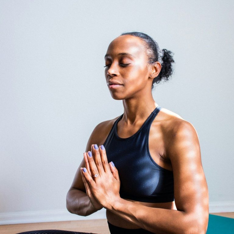 A woman in a black sports top meditating with hands in a prayer position.