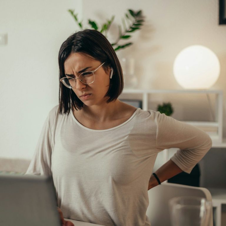Woman sitting at a desk, looking concerned and uncomfortable while working on a laptop..