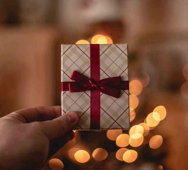 A gift voucher wrapped in patterned paper with a red ribbon, held in front of a lit background.