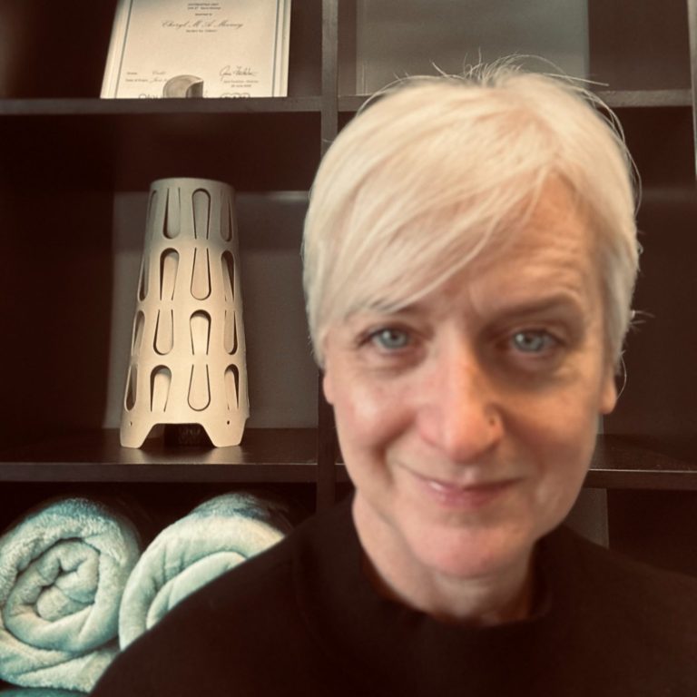 Female massage therapist with short blond hair smiling, in her treatment room at Lotus Moon.