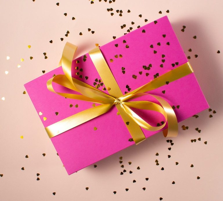 A gift voucher wrapped in patterned paper with a red ribbon, held in front of a lit background.