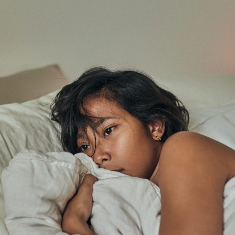 A young person lying on a bed, struggling to get to sleep.