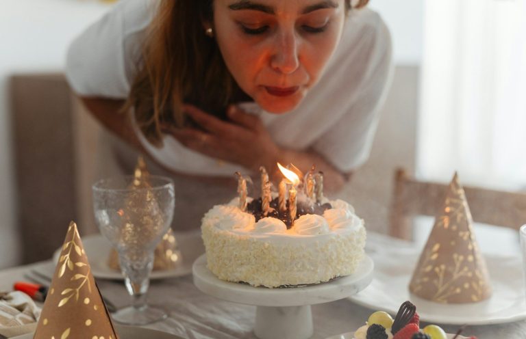 A woman blowing out candles on a birthday cake surrounded by festive decorations.