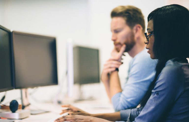 Two people focused on computer screens in a modern workspace.